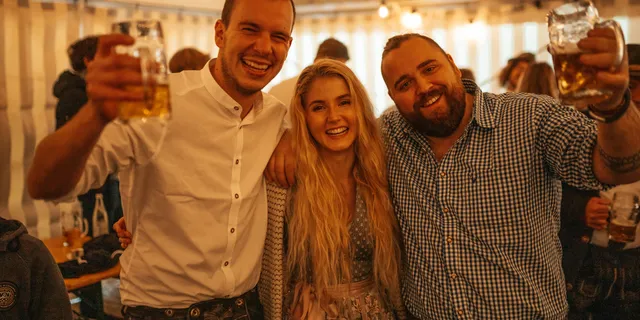 Drei Freunde prosten beim Oktoberfest mit Bierkrügen in die Kamera
