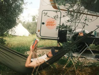 Mann in Hängematte liest Buch vor Wohnmobil