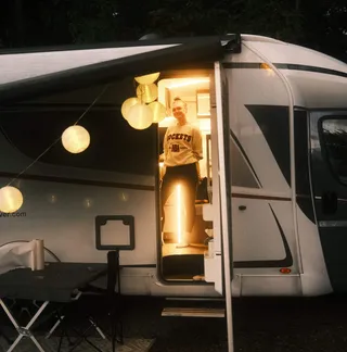 Eine Frau steht in der beleuchteten, geöffneten Aufbautür eines weißen Vanever Wohnmobils Modell Corsica.